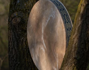 May include: A circular frame drum with a light brown, semi-translucent skin head featuring natural white marbling patterns. The side of the drum frame is decorated with a dark blue and gold intricate repeating geometric knotwork pattern.