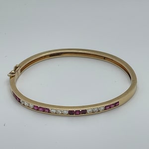 May include: A gold bangle bracelet with a row of small pink gemstones and a row of clear gemstones.