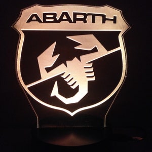 May include: A black and white illuminated sign with the word "ABARTH" and a scorpion logo.