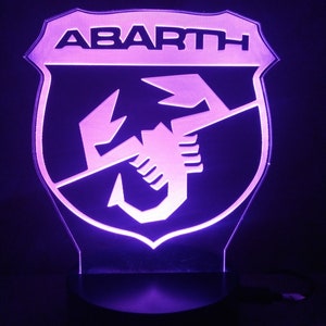 May include: A purple illuminated sign with the word "ABARTH" and a scorpion logo.