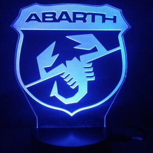 May include: A blue LED light with a white plastic shield featuring the Abarth logo. The logo is a scorpion with the word "ABARTH" above it.