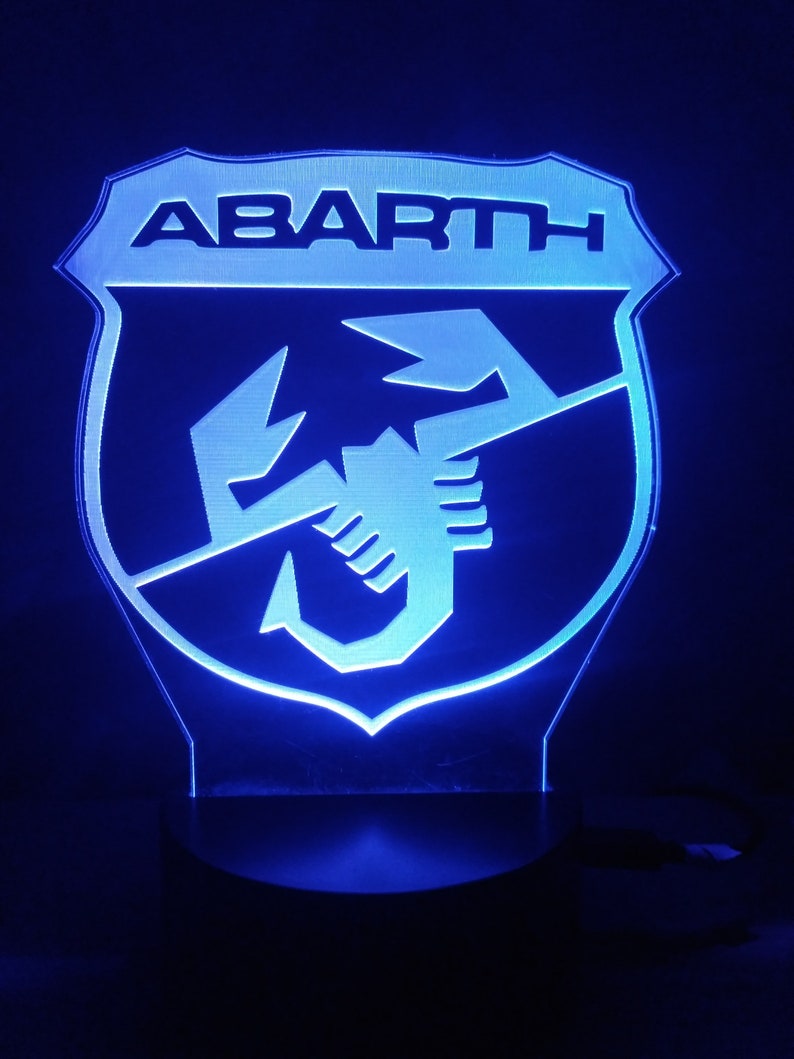 May include: A blue LED light with a white plastic shield featuring the Abarth logo. The logo is a scorpion with the word "ABARTH" above it.