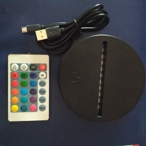 May include: A black round base with a white light strip and a remote control with buttons for different colors, white light, flash, smooth, fade, and mode. The remote control also has buttons for on and off.