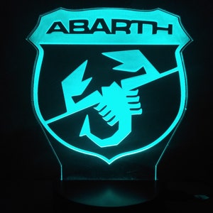 May include: A blue and black illuminated sign with the word "ABARTH" and a scorpion logo.