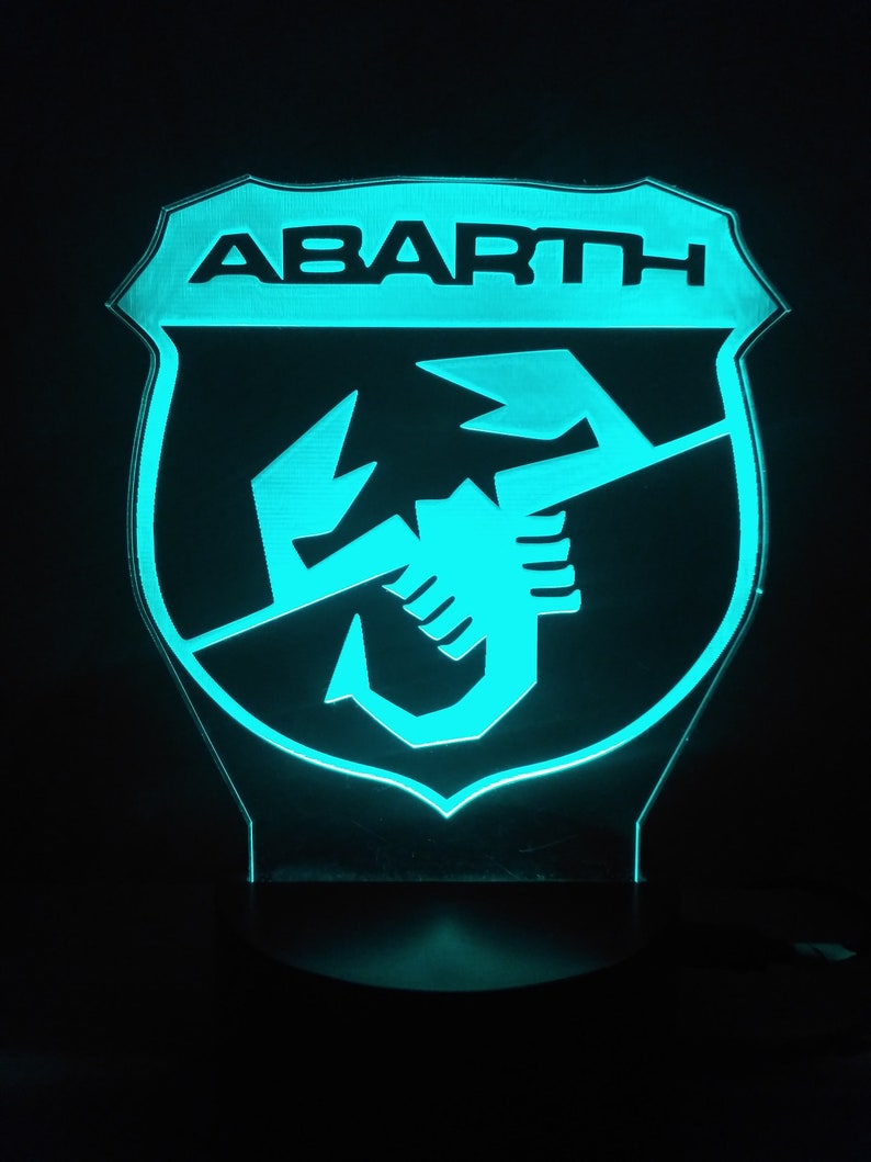 May include: A blue and black illuminated sign with the word "ABARTH" and a scorpion logo.