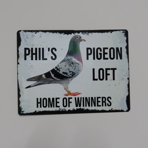 May include: A white metal sign with black text and a black border. The sign says "Phil's Pigeon Loft Home of Winners" and features a photo of a racing pigeon.