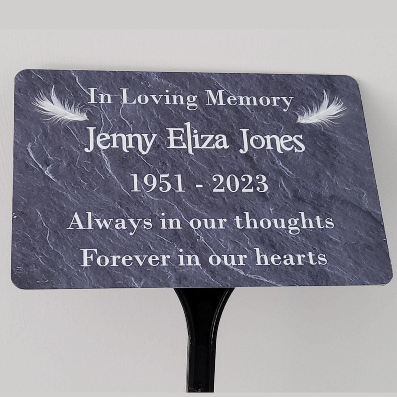 Slate grey effect printed background on metal memorial plaque with white personalised words and two white feathers.  Plaque is attached to a black resin ground stake with an angled head.