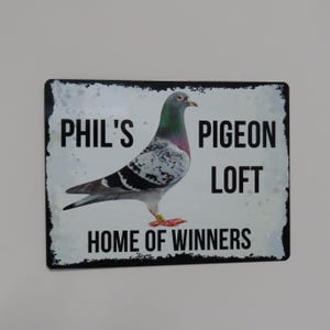 May include: A black and white sign with the text "Phil's Pigeon Loft Home of Winners" and a picture of a pigeon.