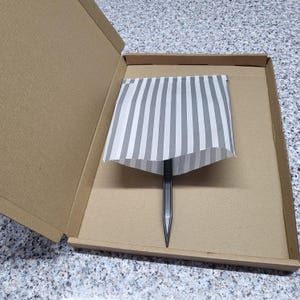 May include: A black pencil is inside a cardboard box with a white and gray striped paper lining.