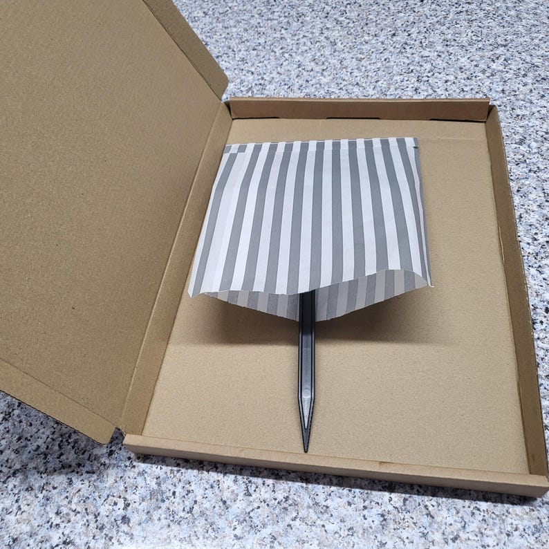May include: A black pencil is inside a cardboard box with a white and gray striped paper lining.