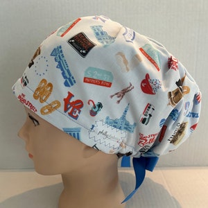 May include: A blue and white patterned surgical scrub hat with a blue ribbon tie. The hat features a variety of Philadelphia-themed icons, including the Reading Terminal Market, Mummers Row, and the Broad Street Run.