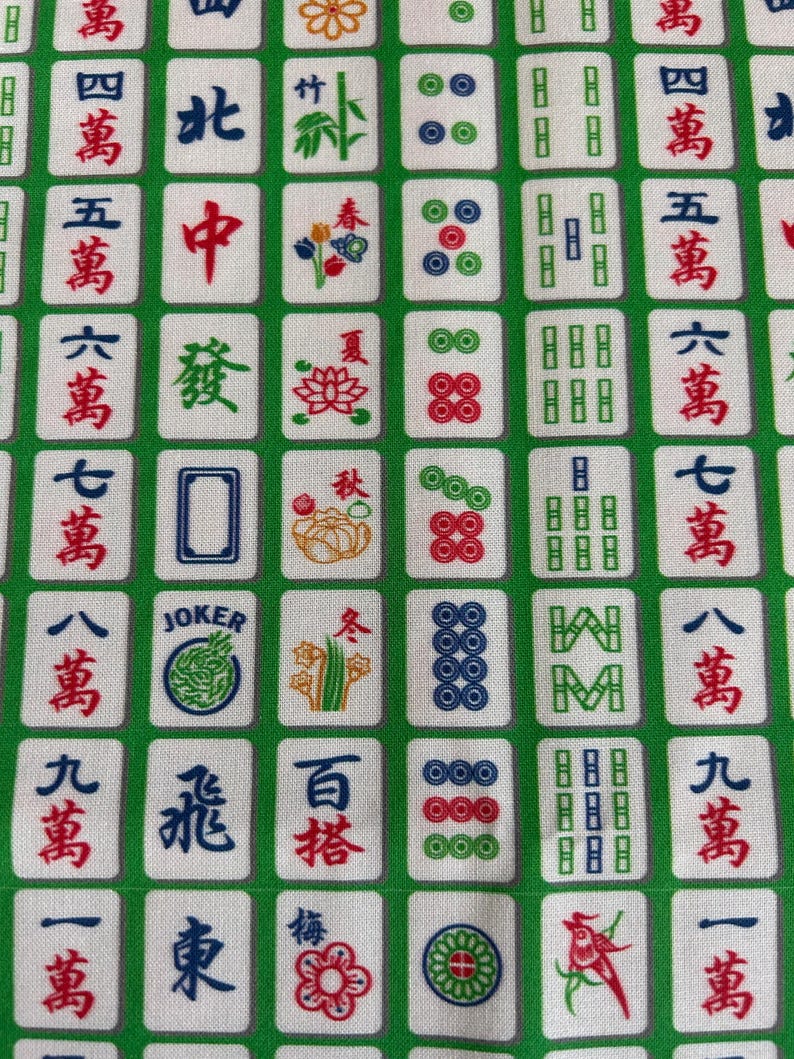 Pode incluir: Uma imagem de perto de um tecido verde e branco com um padr&atilde;o repetido de pe&ccedil;as de Mahjong. As pe&ccedil;as exibem caracteres chineses, n&uacute;meros e s&iacute;mbolos em vermelho, azul e verde. O tecido tem um design semelhante a uma grade.