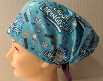 May include: A blue surgical scrub hat with a white and purple print. The hat has a tie on the back and features the text "Laugh, Laryngoscope".