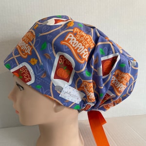 May include: A blue surgical scrub cap with a repeating pattern of pumpkin spice labels and fall leaves. The text "Pumpkin Spice Propofol" is printed in orange. The cap has an orange tie and a small tag that says "phillyfabrics".