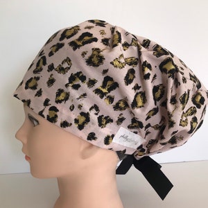 May include: A pink scrub cap with a gold and black leopard print. The cap has a black tie and a white label that says "phillyfabrics".
