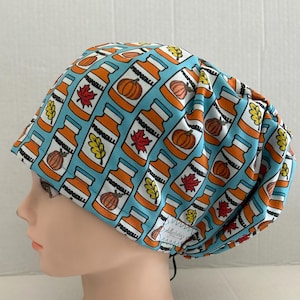 May include: A blue surgical scrub cap with a repeating pattern of orange bottles, pumpkins, and fall leaves. The bottles have the word "PROPOSEALL" printed on them. The cap is made of a soft fabric and has a black drawstring.
