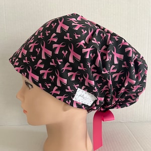 May include: Black scrub hat with a pink ribbon pattern. The hat has a tie at the back and a small label that says "phillyfabrics".