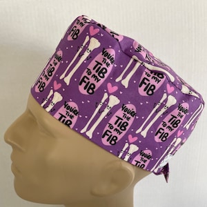 May include: Purple scrub hat with a repeating pattern of white bones and pink hearts. The text "You're the Tib to my Fib" is repeated on the hat.
