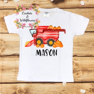 May include: White t-shirt with a red and yellow watercolor illustration of a combine harvester with pumpkins. The text "MASON" is printed below the image.