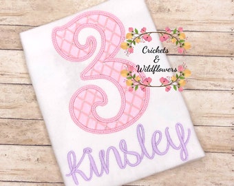 May include: A white t-shirt with a pink number 3 with a diamond pattern and the name "Kinsley" embroidered in purple.