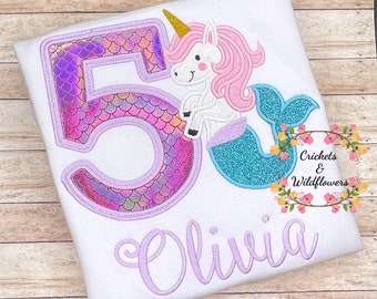 May include: A white t-shirt with a purple number 5 with iridescent scales, a mermaid unicorn with pink hair and a turquoise tail, and the name Olivia embroidered in purple.