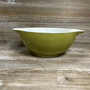 May include: A vintage olive green mixing bowl with a white interior. The bowl has a rounded shape with a flared rim and a handle-like spout on either side. The bowl is made of a durable material.