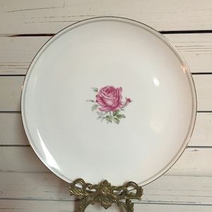 Puede incluir: Plato de cena de cerámica blanca con borde dorado y diseño de rosa rosa.