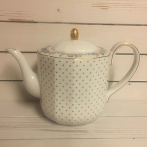 May include: White teapot with a gold star pattern and a floral design around the rim. The teapot has a gold knob on the lid.