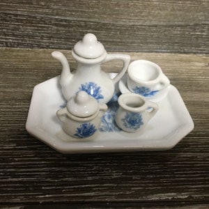 May include: A white porcelain tea set with blue floral designs. The set includes a teapot, creamer, sugar bowl, cup and saucer. The set is on a white tray.