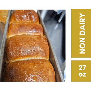 May include: A close-up of a metal baking pan filled with four golden-brown, non-dairy rolls. The rolls are rectangular and have a glossy finish. The image includes a gold rectangle with the words "NON DAIRY" and "27 oz".