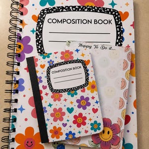 Op de afbeelding: Een groot spiraalgebonden notitieboek en een kleiner rechthoekig notitieboek met een witte achtergrond met kleurrijke bloemen, harten en sterren. Beide notitieboeken hebben een zwart-wit gespikkeld label met de tekst COMPOSITION BOOK.
