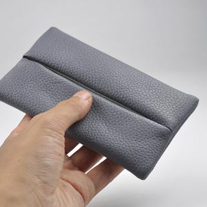 Pu&ograve; includere: Una custodia rettangolare grigia con una superficie testurizzata e granulosa. La custodia presenta un'apertura orizzontale centrale che corre lungo tutta la lunghezza dell'articolo, creando due lembi sovrapposti che si incontrano al centro.