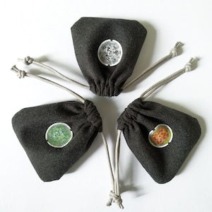 Puede incluir: Cuatro pequeñas bolsas de cordón gris con diseños circulares de diferentes colores en la parte delantera. Los diseños son un círculo gris, un círculo verde, un círculo amarillo y un círculo naranja.