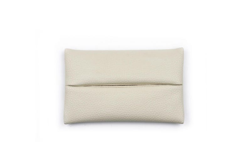 Pu&ograve; includere: Un copriscatola per fazzoletti rettangolare color bianco sporco con una superficie testurizzata e granulosa. Il copriscatola presenta una fessura orizzontale al centro, progettata per estrarre i fazzoletti nascondendo la scatola sottostante.