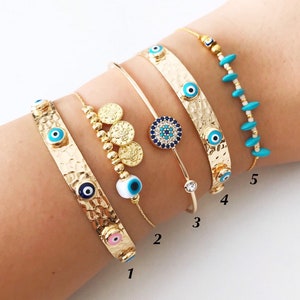 May include: Five gold bracelets with blue evil eye charms. The bracelets are stacked on a person's wrist. The bracelets are numbered 1 through 5.