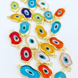 May include: Assortment of colorful evil eye charms with gold accents. The charms are oval shaped with a blue eye in the center.