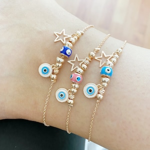 Peut inclure: Trois chevillères dorées avec des breloques œil maléfique et des breloques étoiles. Les chevillères ont des breloques œil maléfique bleu, rose et bleu clair.