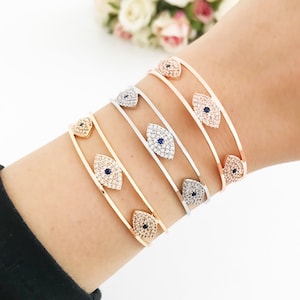 May include: Four gold, silver, and rose gold bracelets with a blue evil eye charm. Each bracelet is adorned with clear cubic zirconia stones.