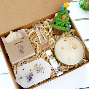 Könnte beinhalten: Eine Geschenkbox mit Lavendelseife, einer Kerze, Lippenbalsam, Streichhölzern und einem gehäkelten Weihnachtsbaum. Die Seife ist mit "Lavendel" beschriftet und die Kerze befindet sich in einer Metalldose. Die Box ist mit Papier gefüllt.