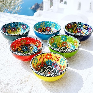 Puede incluir: Un conjunto de seis cuencos pequeños de cerámica con vibrantes patrones florales multicolores y diseños intrincados pintados a mano. Cada cuenco muestra un esquema de color único, incluyendo rojo, amarillo, verde, azul y negro, con detalles blancos.
