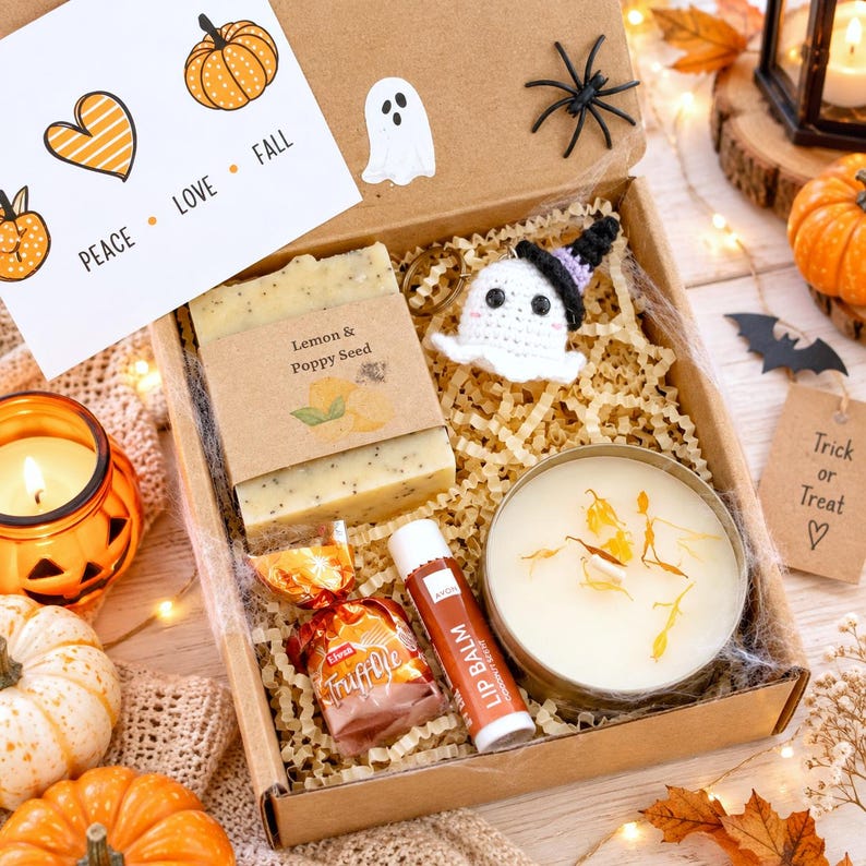 May include: A cardboard gift box containing a bar of lemon and poppy seed soap, a round tin candle with dried petals, a tube of lip balm, a wrapped truffle, and a crocheted ghost keychain. A card inside reads PEACE LOVE FALL.