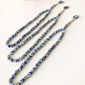May include: Three blue and white evil eye bead necklaces with silver accents. The necklaces are strung on a silver chain.