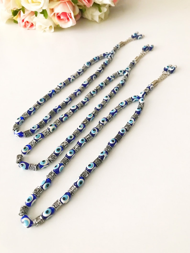 May include: Three blue and white evil eye bead necklaces with silver accents. The necklaces are strung on a silver chain.