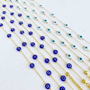 May include: A set of gold chain necklaces with blue and white evil eye charms. The necklaces are arranged in a row, with the shortest necklace at the top and the longest necklace at the bottom.
