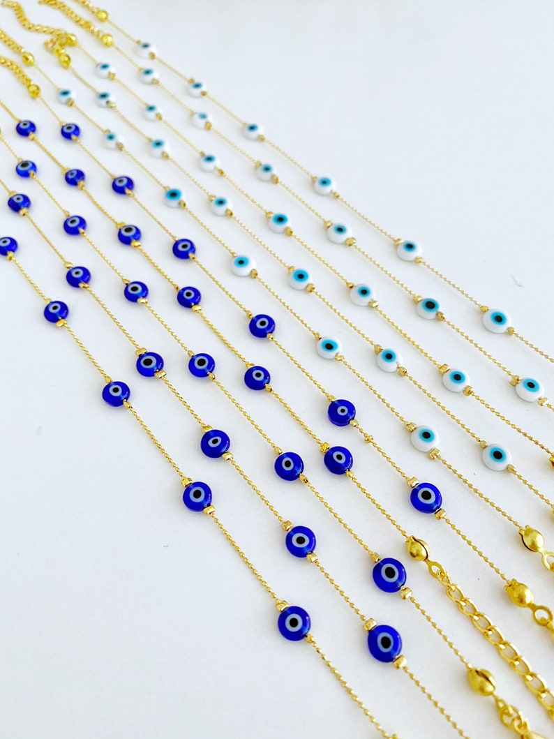 May include: A set of gold chain necklaces with blue and white evil eye charms. The necklaces are arranged in a row, with the shortest necklace at the top and the longest necklace at the bottom.