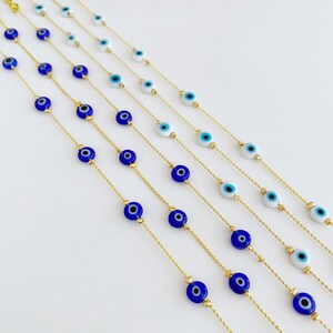 May include: A set of six gold chain bracelets with blue and white evil eye charms. The bracelets are layered and arranged in a fan shape.