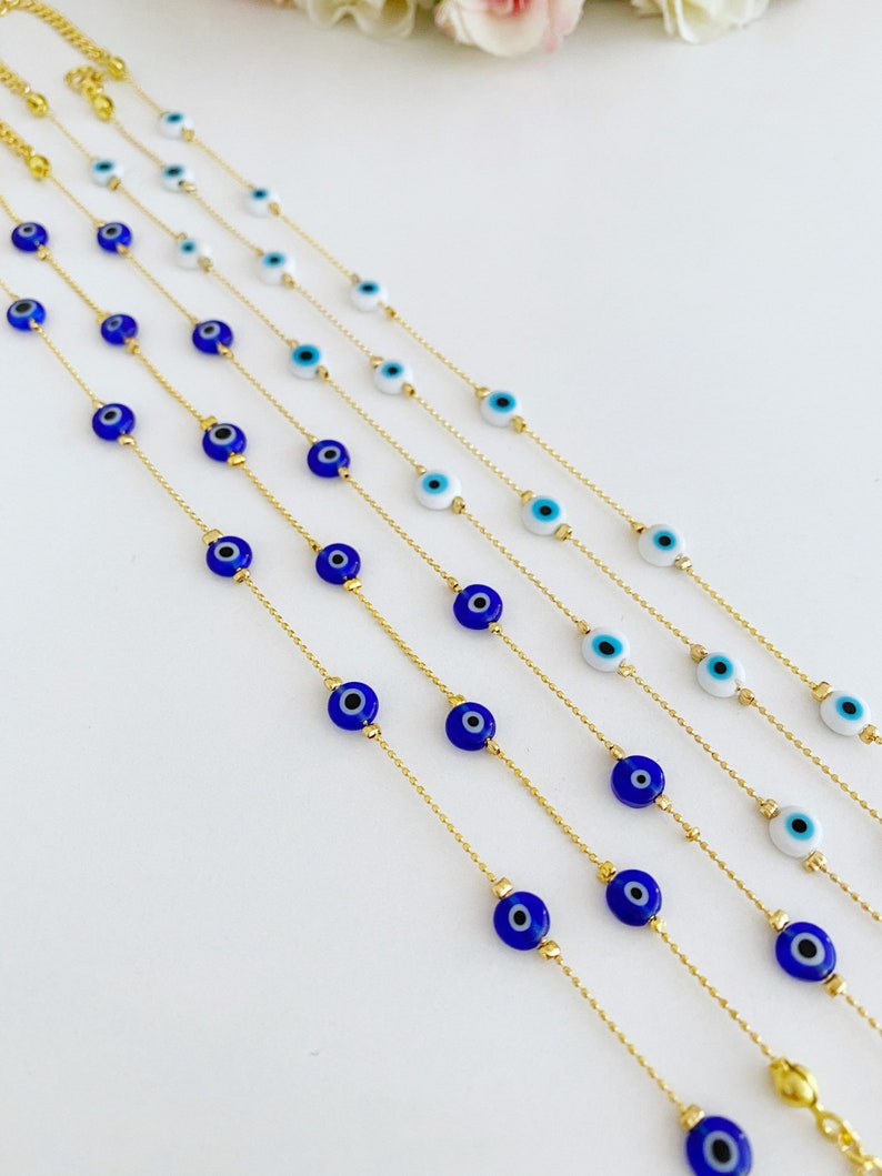 May include: A set of six gold chain bracelets with blue and white evil eye charms. The bracelets are layered and arranged in a fan shape.