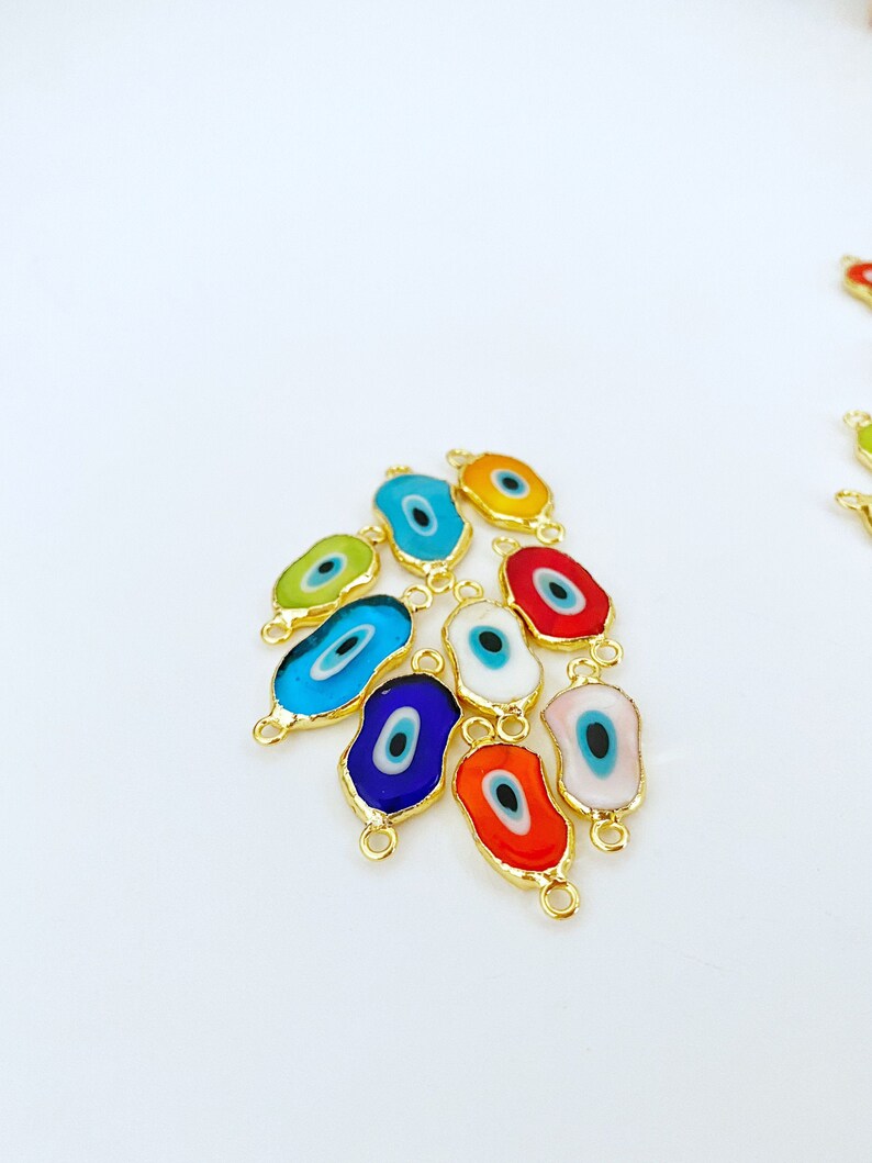 May include: Assortment of colorful evil eye charms with gold accents. Each charm features a blue eye with a white pupil and is surrounded by a different colored enamel. The charms have two gold jump rings for attaching to jewelry.