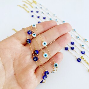May include: A set of gold chain necklaces with blue and white evil eye beads. The necklaces are layered on a hand.