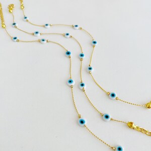 May include: Three gold chains with blue and white evil eye charms. The chains are layered on a white surface.